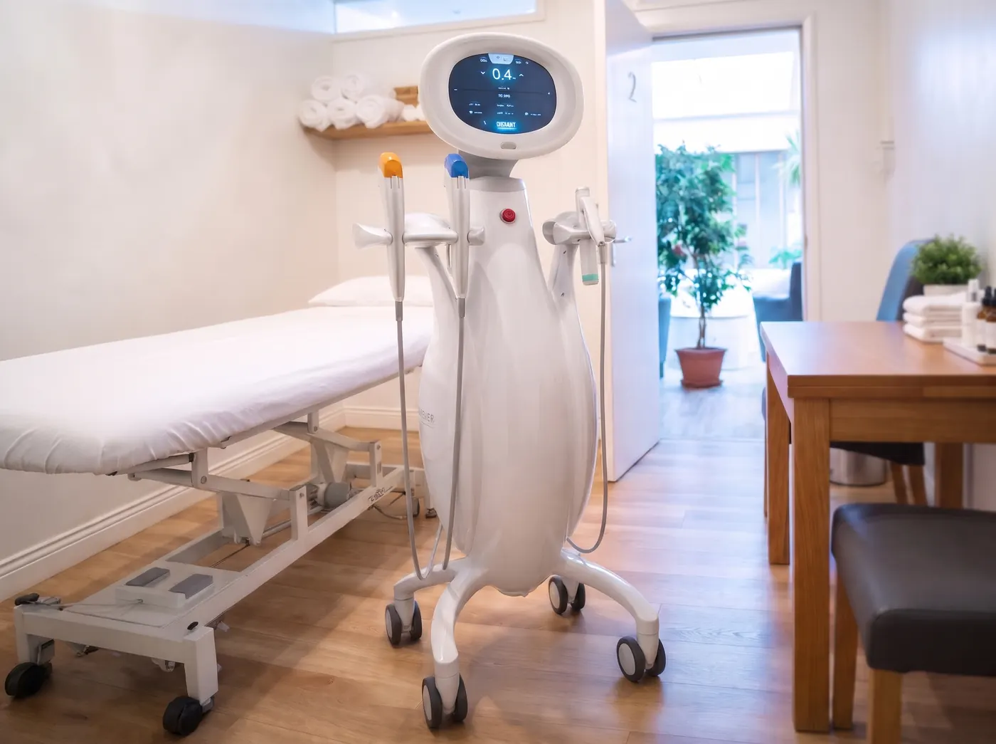 The Ultraformer MPT: a white sculpted console with a round screen and its handpieces in holders, beside a treatment couch