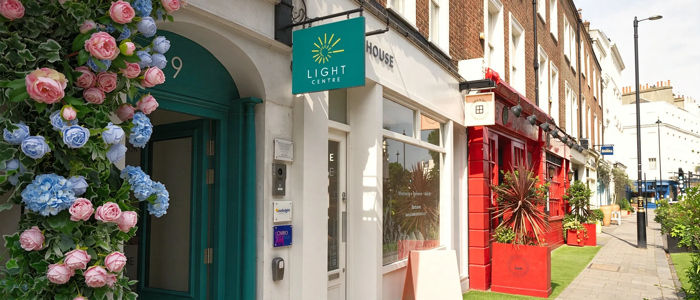 The teal entrance of The Light Centre on Eccleston Street, framed by roses and hydrangeas, with its hanging sign